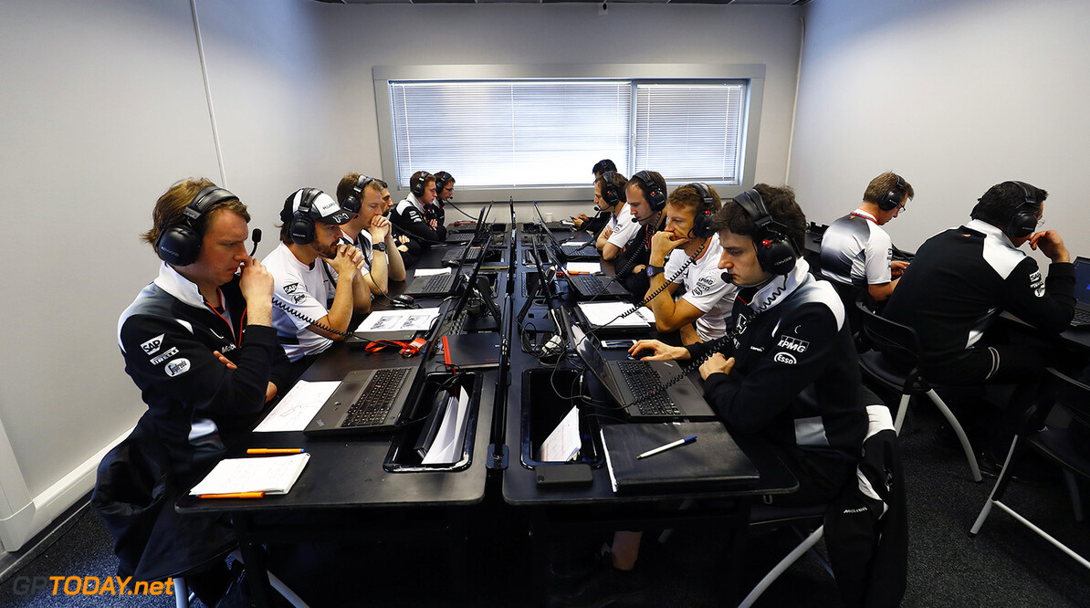 Jenson Button and Fernando Alonso study data with team members.